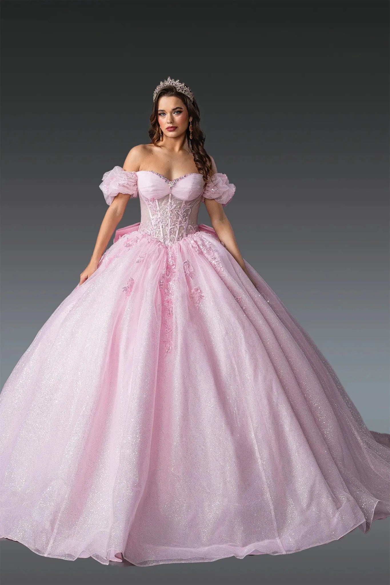 Woman standing front-facing in blush sparkling ball gown skirt fabric with layered tulle and embroidered detailing from off-shoulder quinceañera dress