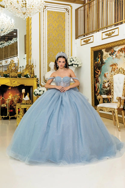 Woman standing front-facing in dusty blue strapless quinceañera dress with off-shoulder sleeves, sheer corset bodice, and sparkling voluminous ball gown skirt