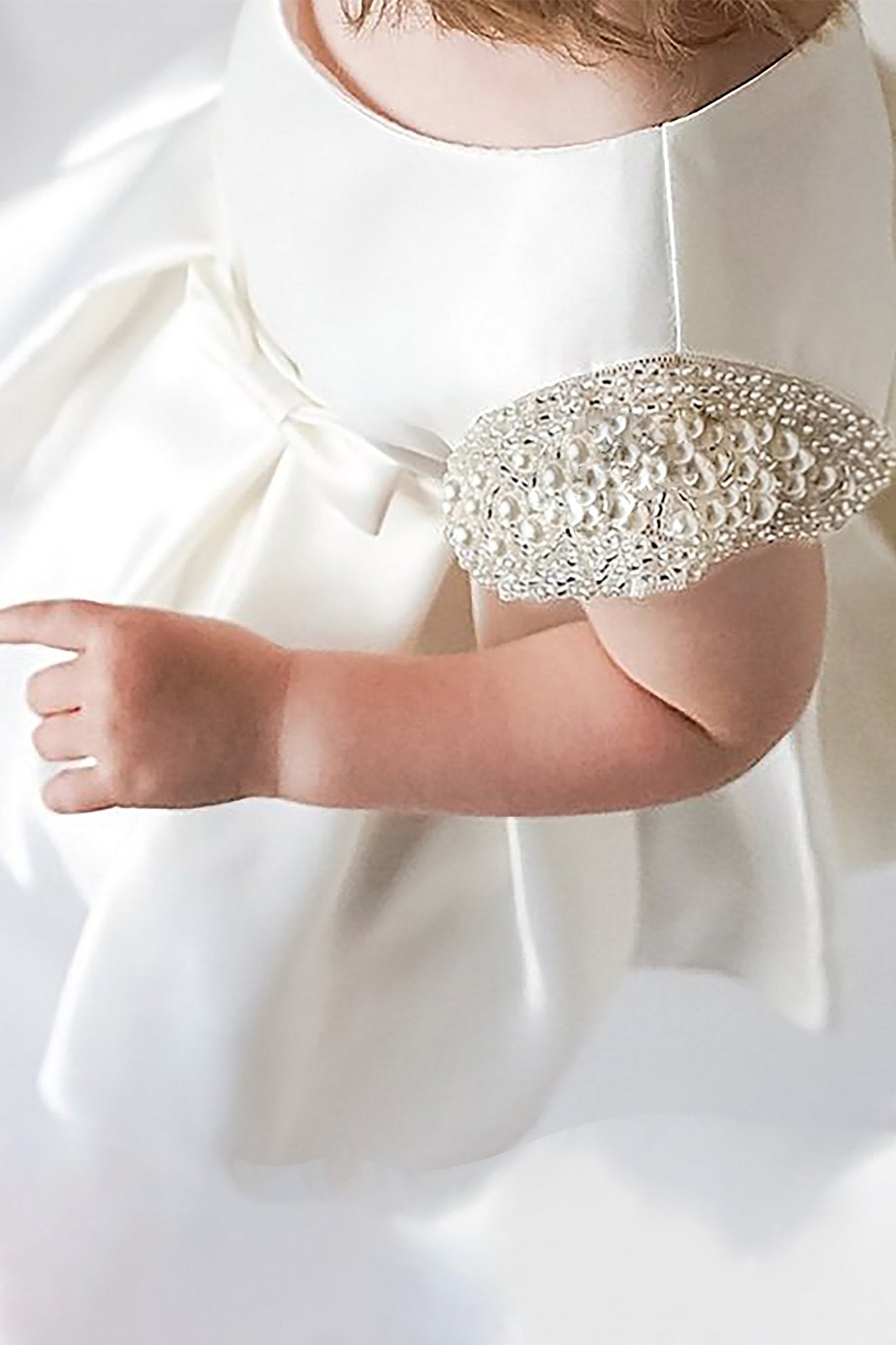Close-up of a ivory flower girl dress with embellished elbow pads.