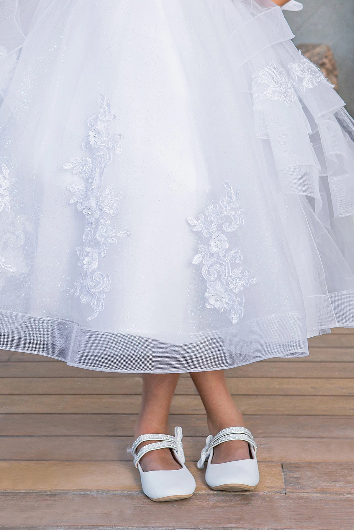 Layered tulle and flower appliques shape the White communion dress hem.