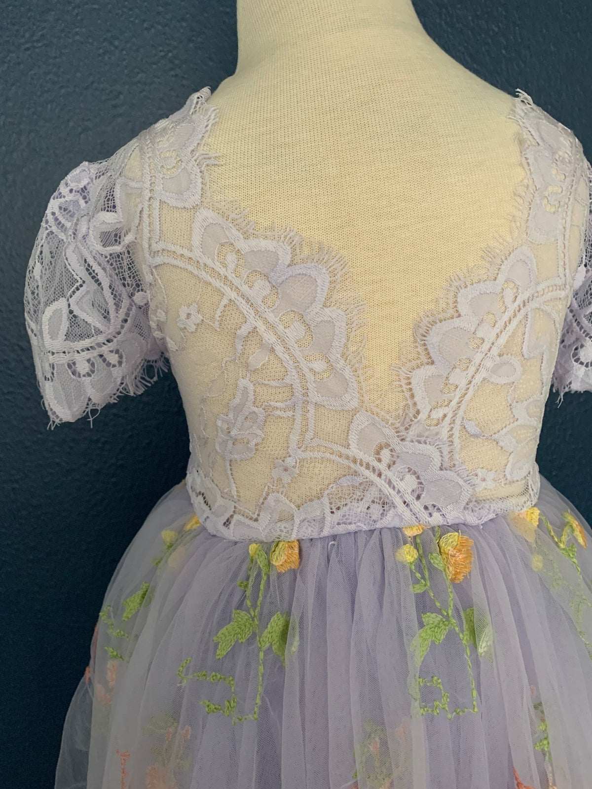 Close-up of a lilac V back flower girl dress with lace detailing.