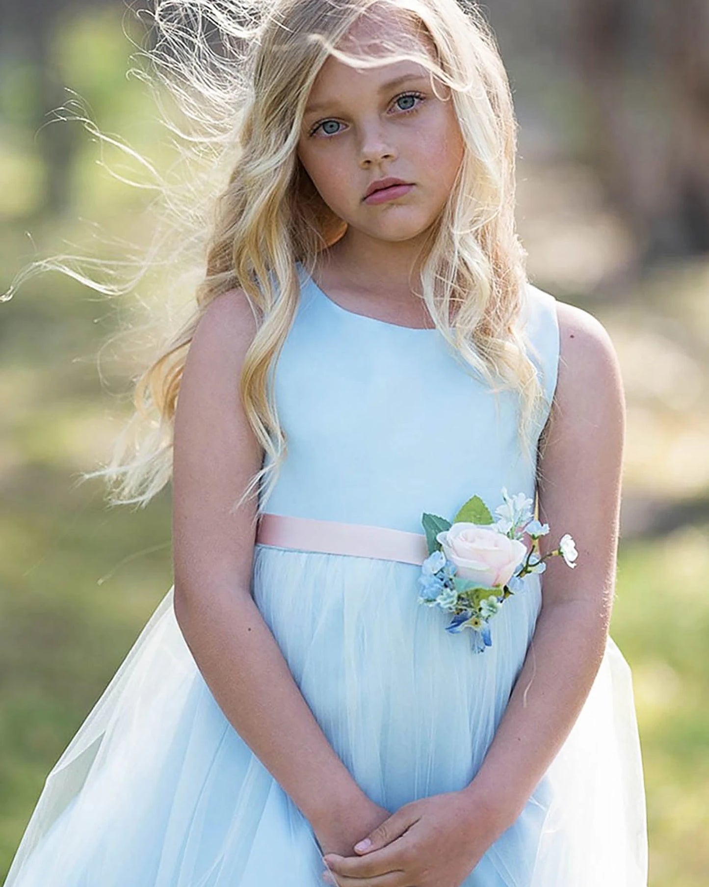 A light blue flower girl dress with a pink belt and flower bouquet.
