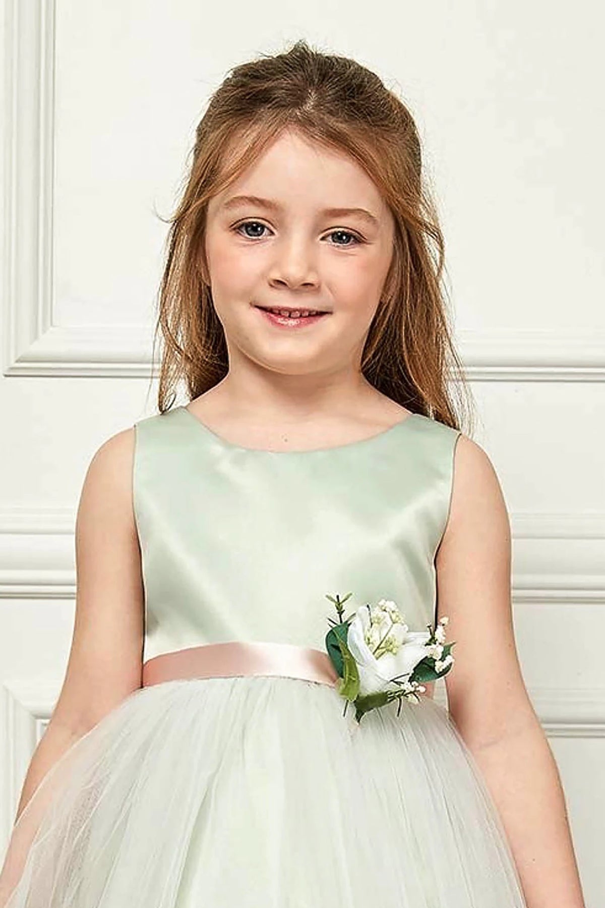 Textured details appear across a light green flower girl dress with a white flower corsage.