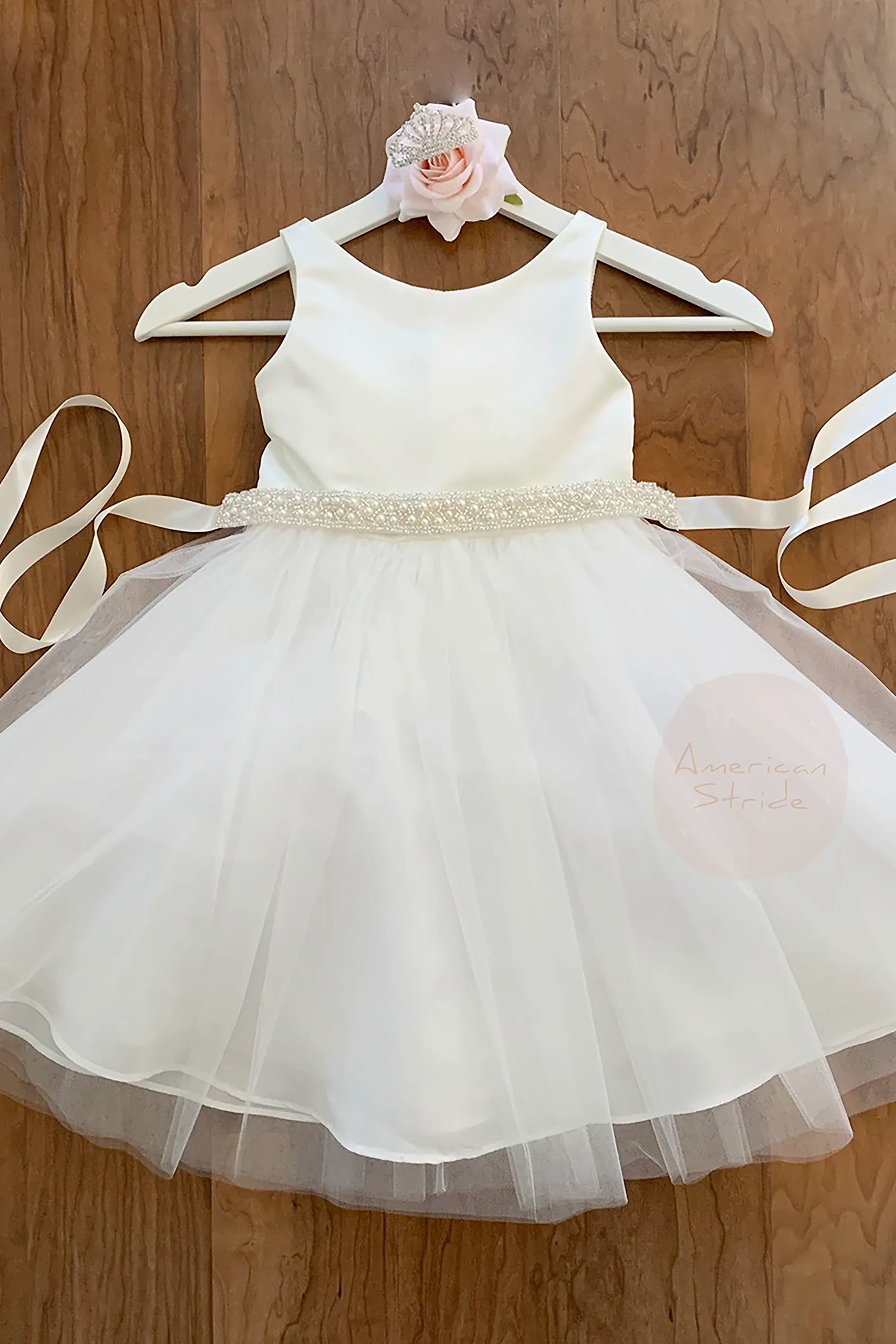 off white satin top and tull skirt kid dress with ivory pearl sash on a wood background