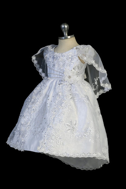Detail of the white christening dress showing metallic Virgin Mary embroidery and a split organza skirt.