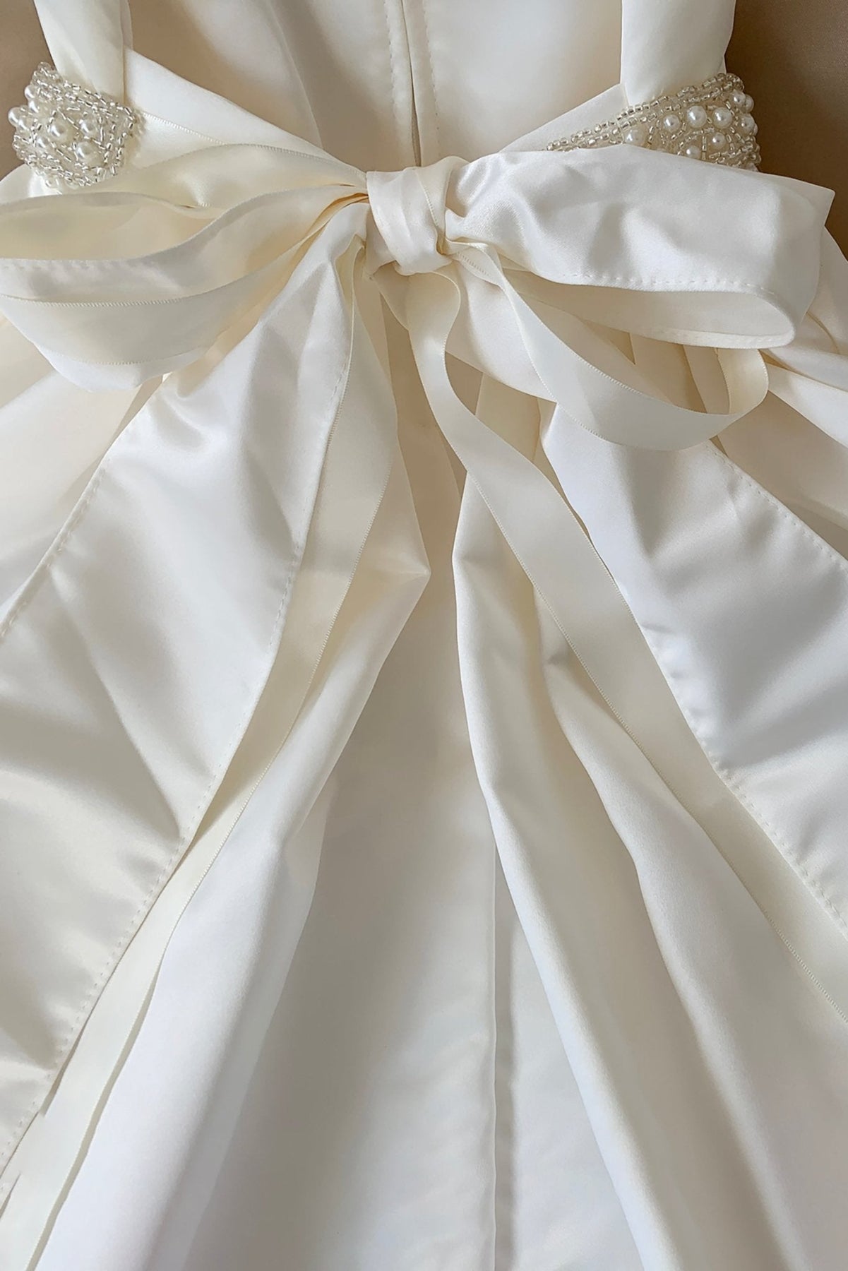 Close-up of a white flower girl dress with a large bow detail. Also suitable as a communion dress. Also suitable as a baptism dress.