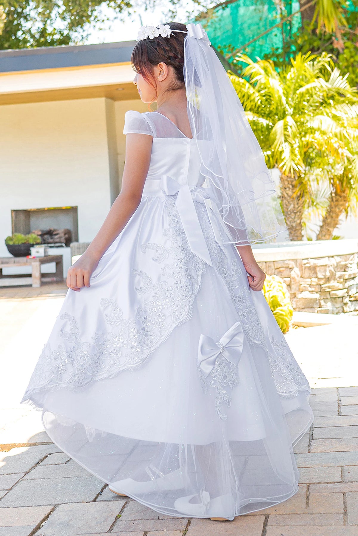Layered lace falls below the back bow on this White communion dress.