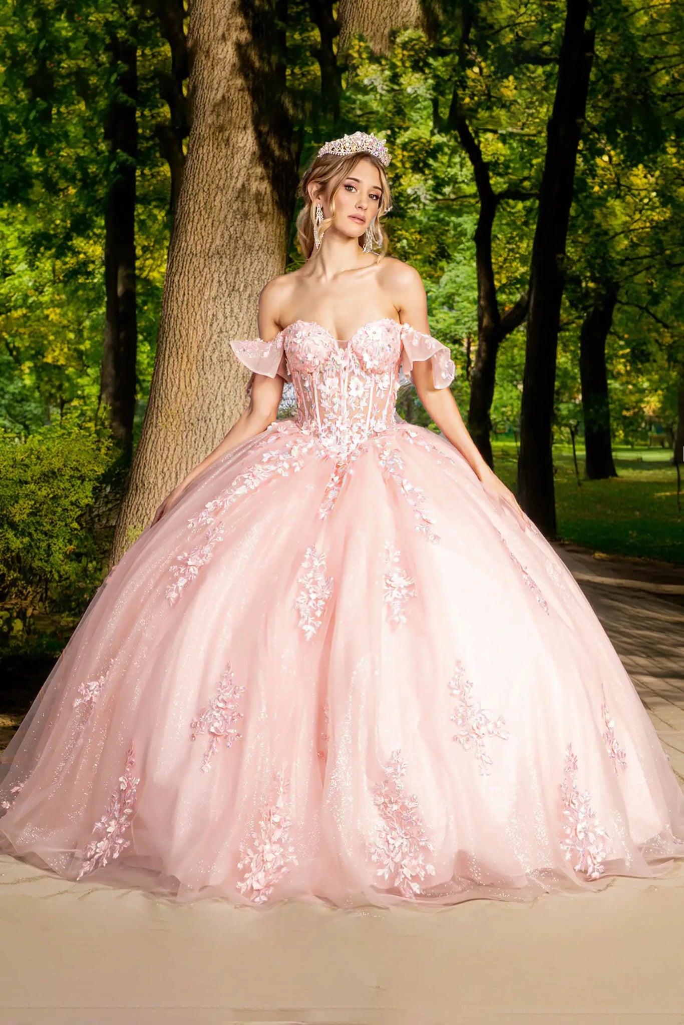 Woman in a pink gown standing in a park with trees and grass in the background