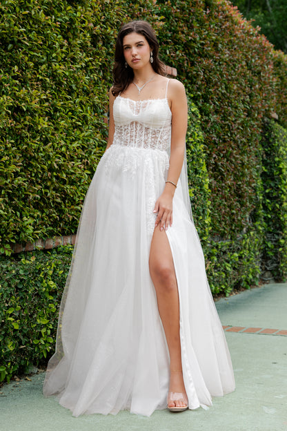Woman wearing a white dress with a high slit in front of green foliage.