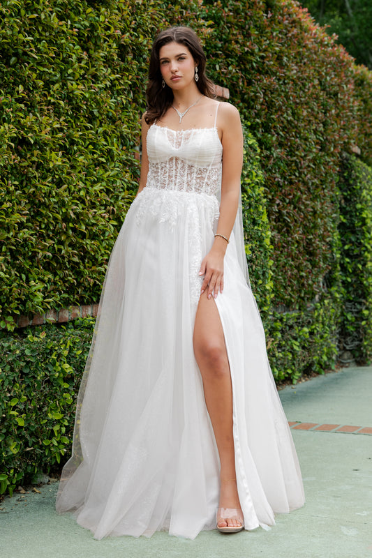 Woman wearing a white dress with a high slit in front of green foliage.