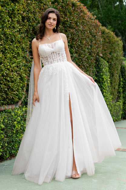 Woman in a white strapless gown with a high slit standing outdoors against greenery.