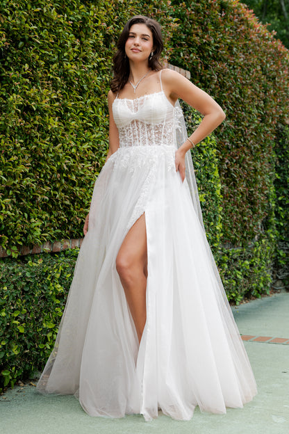 Woman in a white dress with a high slit standing in front of green hedges.