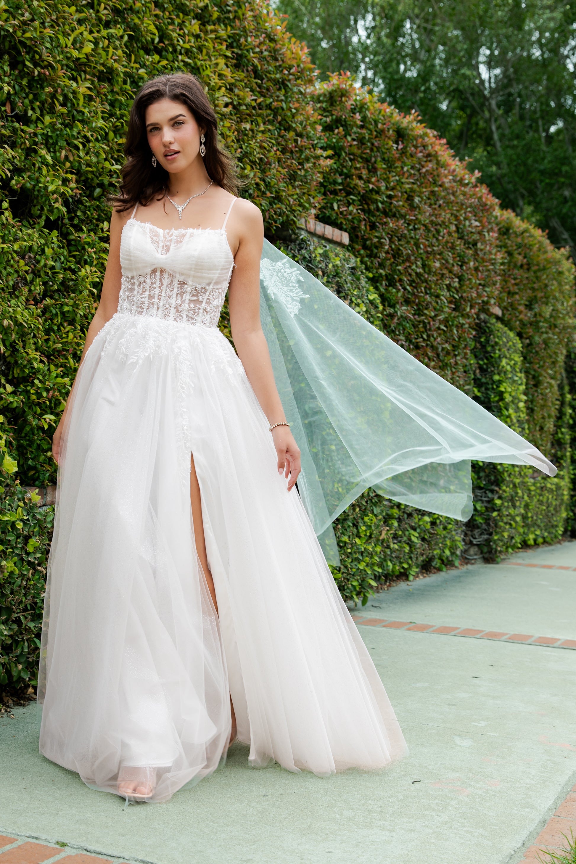 Woman in a white dress with a green veil standing in front of greenery