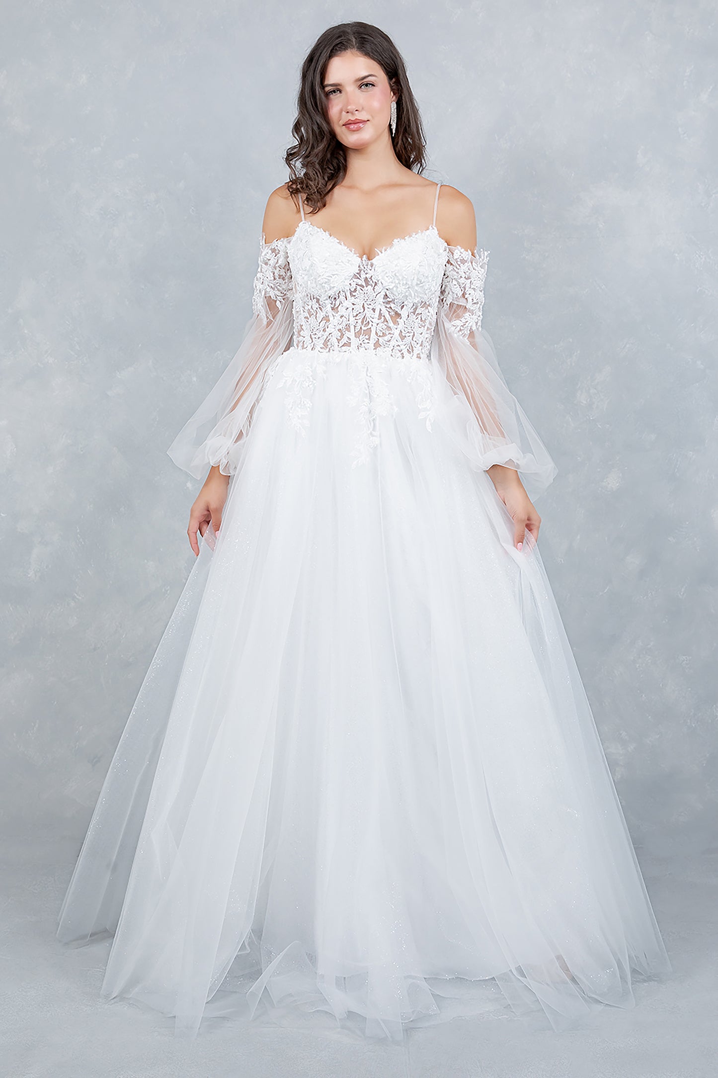 Woman wearing a white wedding dress with lace top and sheer sleeves against a gray background