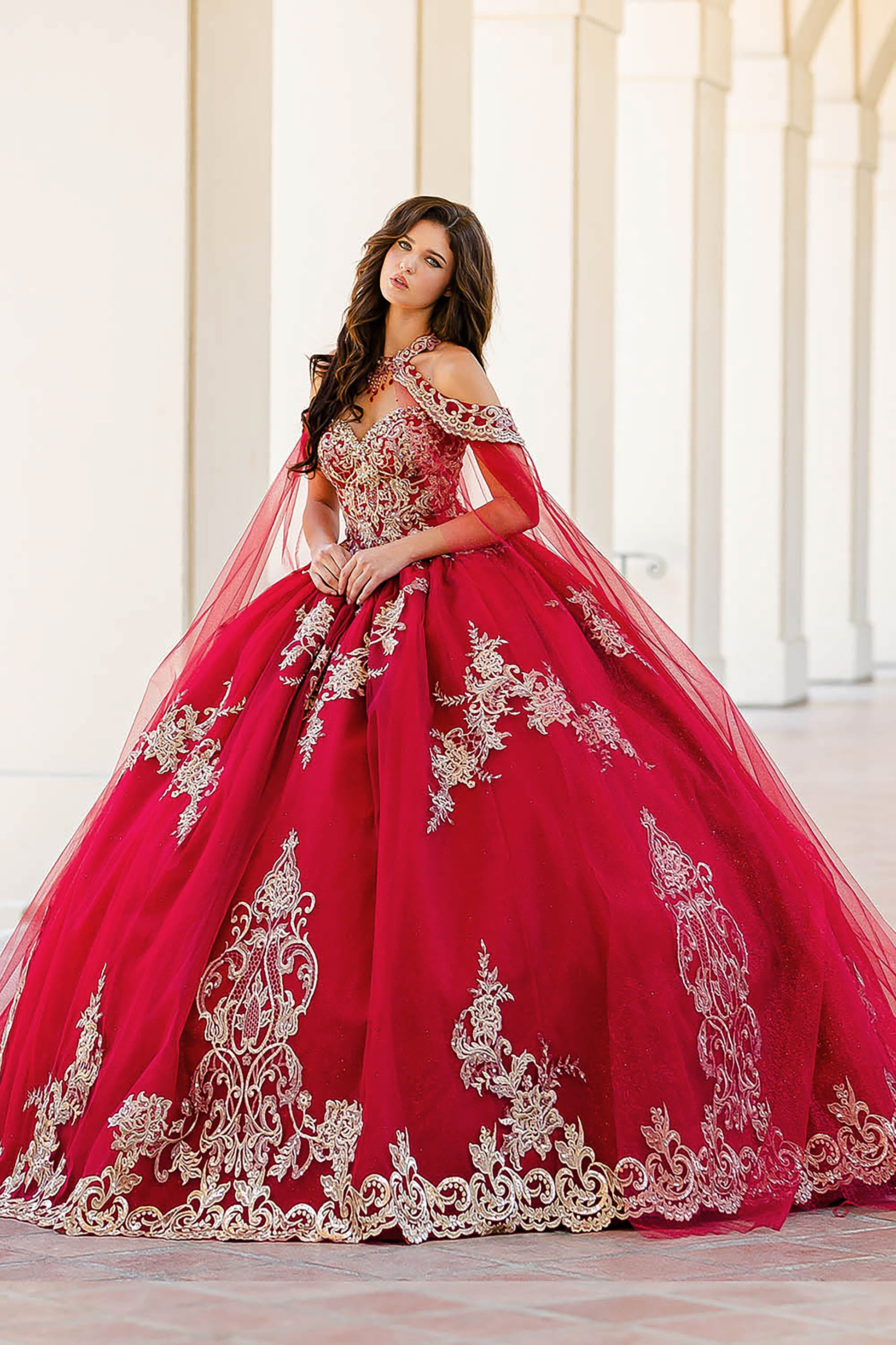 Quinceanera | Wine with Gold Embroidered Lace with Stunning Cape Quince Ballgown dress - front view of woman wearing dress slightly turned to the side with both hands clasped in the front