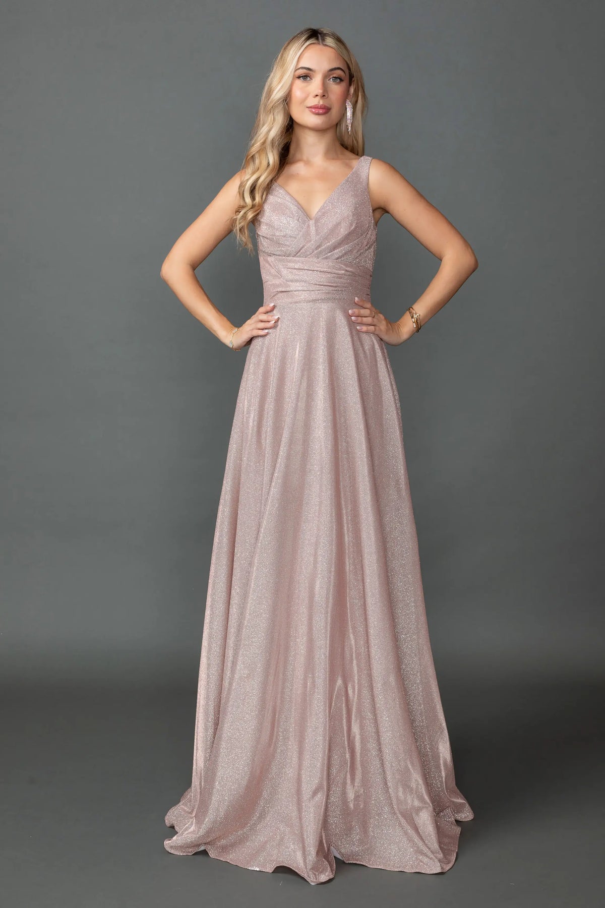 Showing a ruched V-neck bodice and flowing glitter skirt, this Rose Gold prom dress is shown in full view.