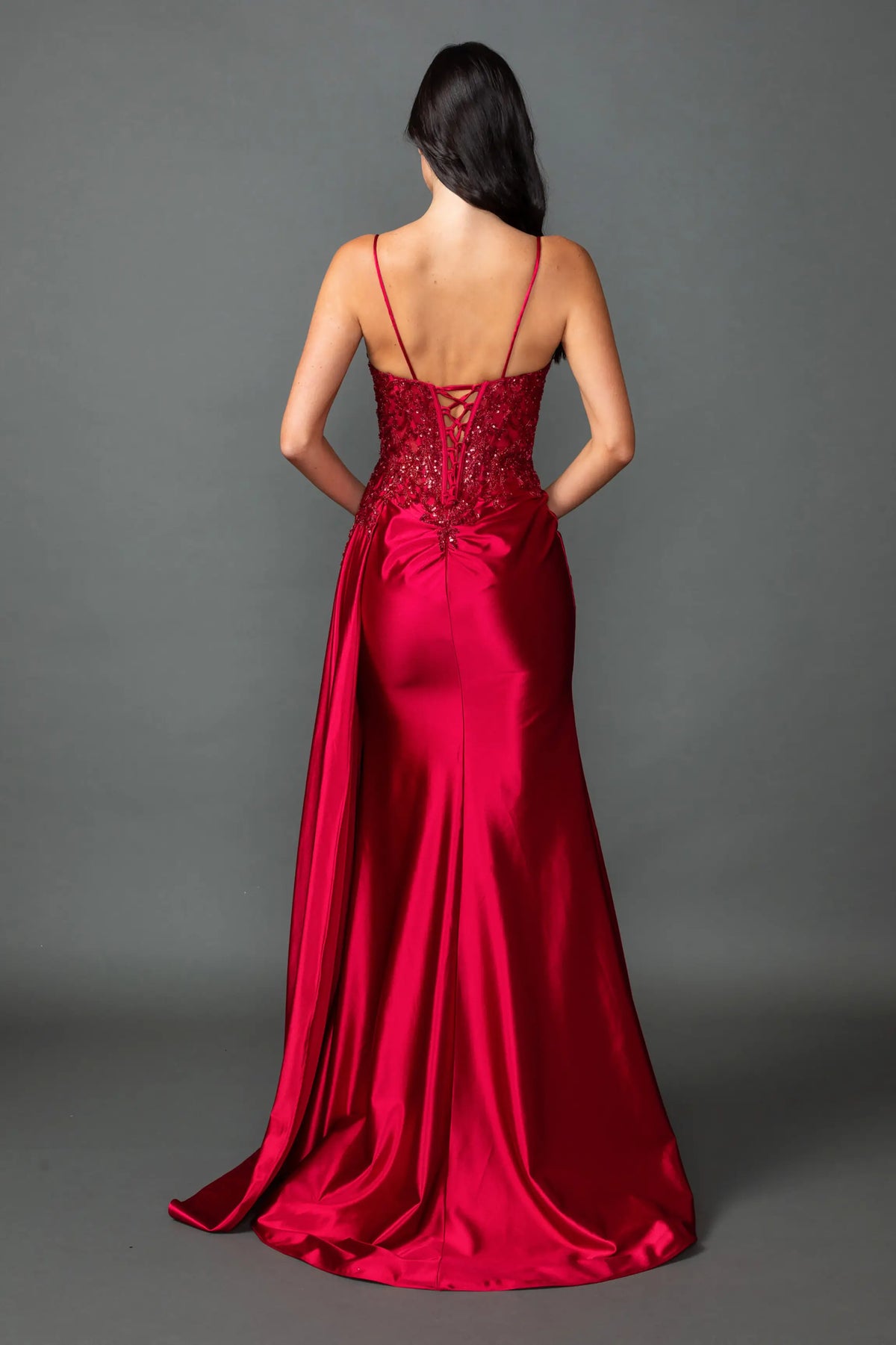 Revealing corset lacing above its satin train, this Burgundy prom dress is shown from the back.