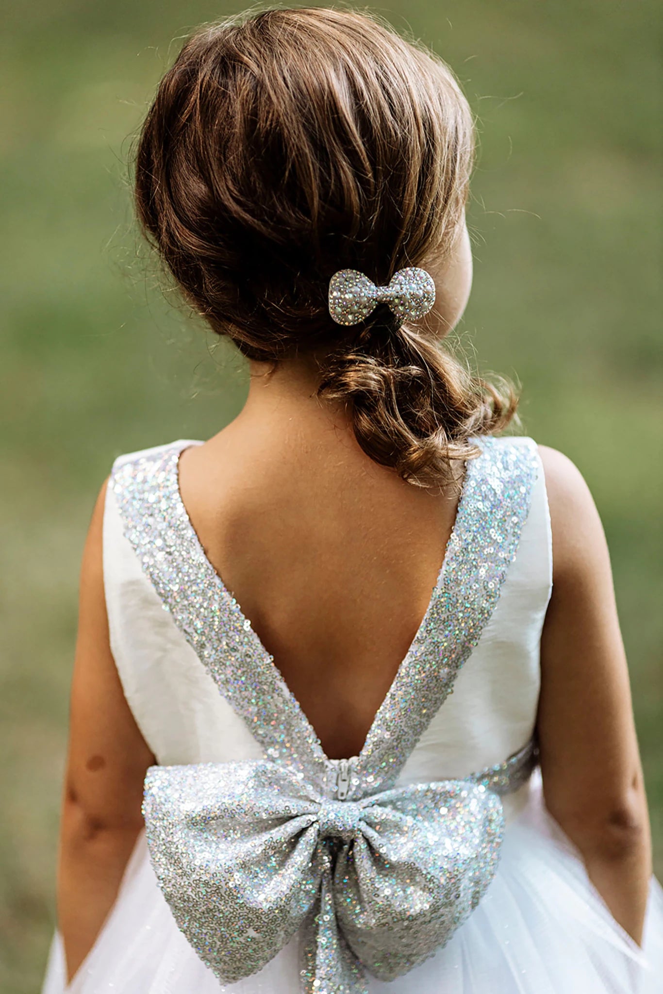 Back view of a white flower girl dress with a large silver bow.