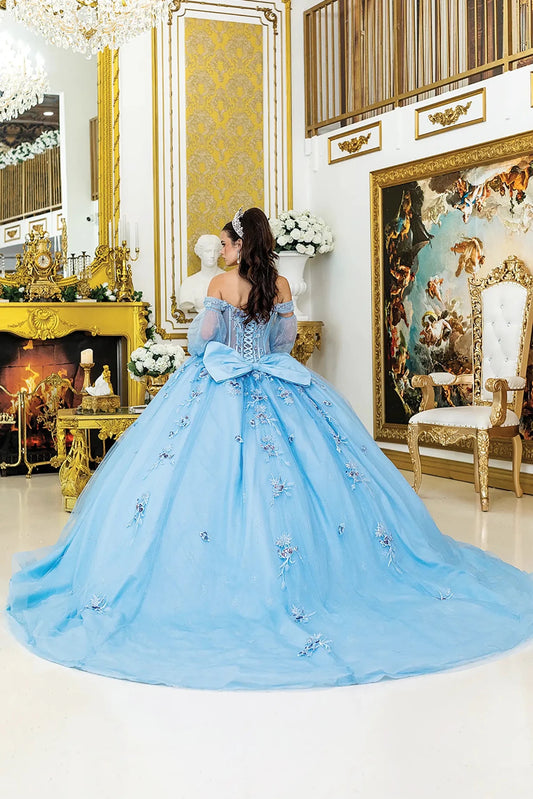 Woman standing back-facing in Bahama blue quinceañera ball gown with lace-up corset bodice, sheer off-shoulder sleeves, floral appliqués, and flowing glitter tulle skirt with train