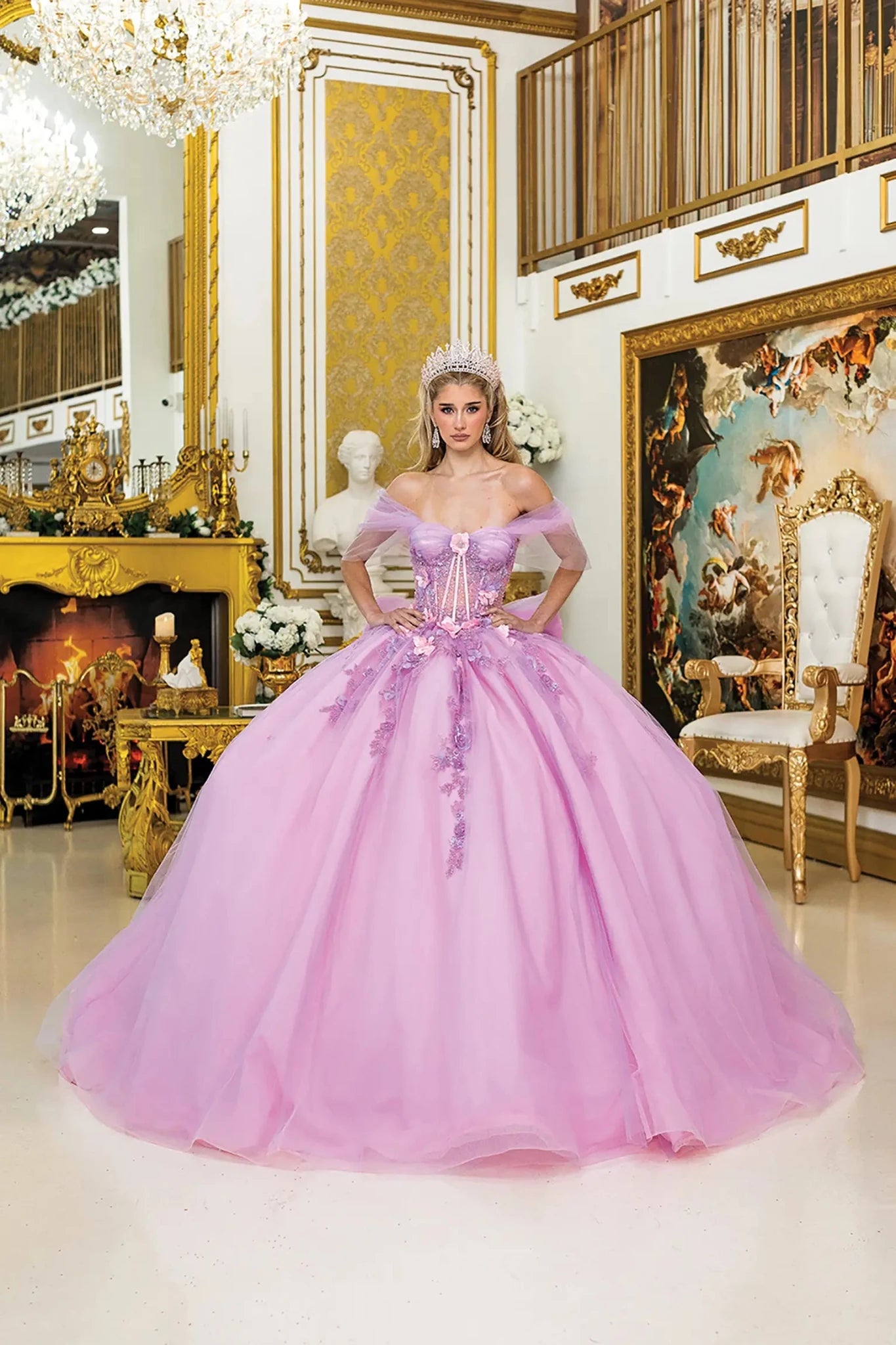 Woman standing front-facing in lilac-blush quinceañera ball gown with off-shoulder sheer sleeves, corset bodice, floral embroidery, 3D appliqués, and voluminous layered tulle skirt
