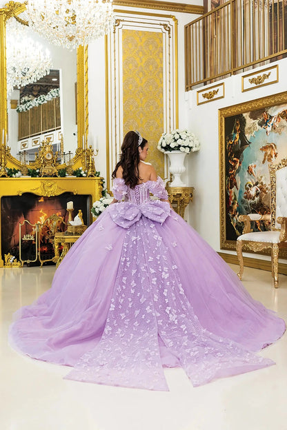 Woman standing back-facing in lilac quinceañera ball gown with lace-up sheer corset bodice, off-shoulder sleeves, floral 3D appliqués, and flowing glitter tulle skirt with train