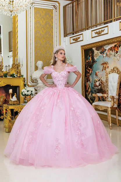 Woman standing front-facing in pink quinceañera ball gown with off-shoulder sleeves, fitted bodice, floral appliqués, and voluminous layered tulle skirt