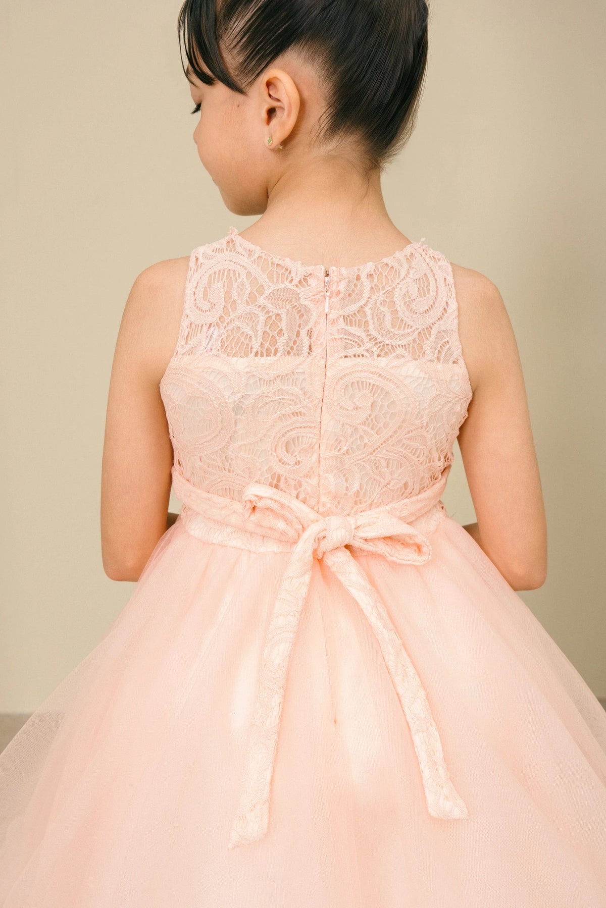Detailed by a lace back and satin bow, the Peach kids party dress reveals its construction.