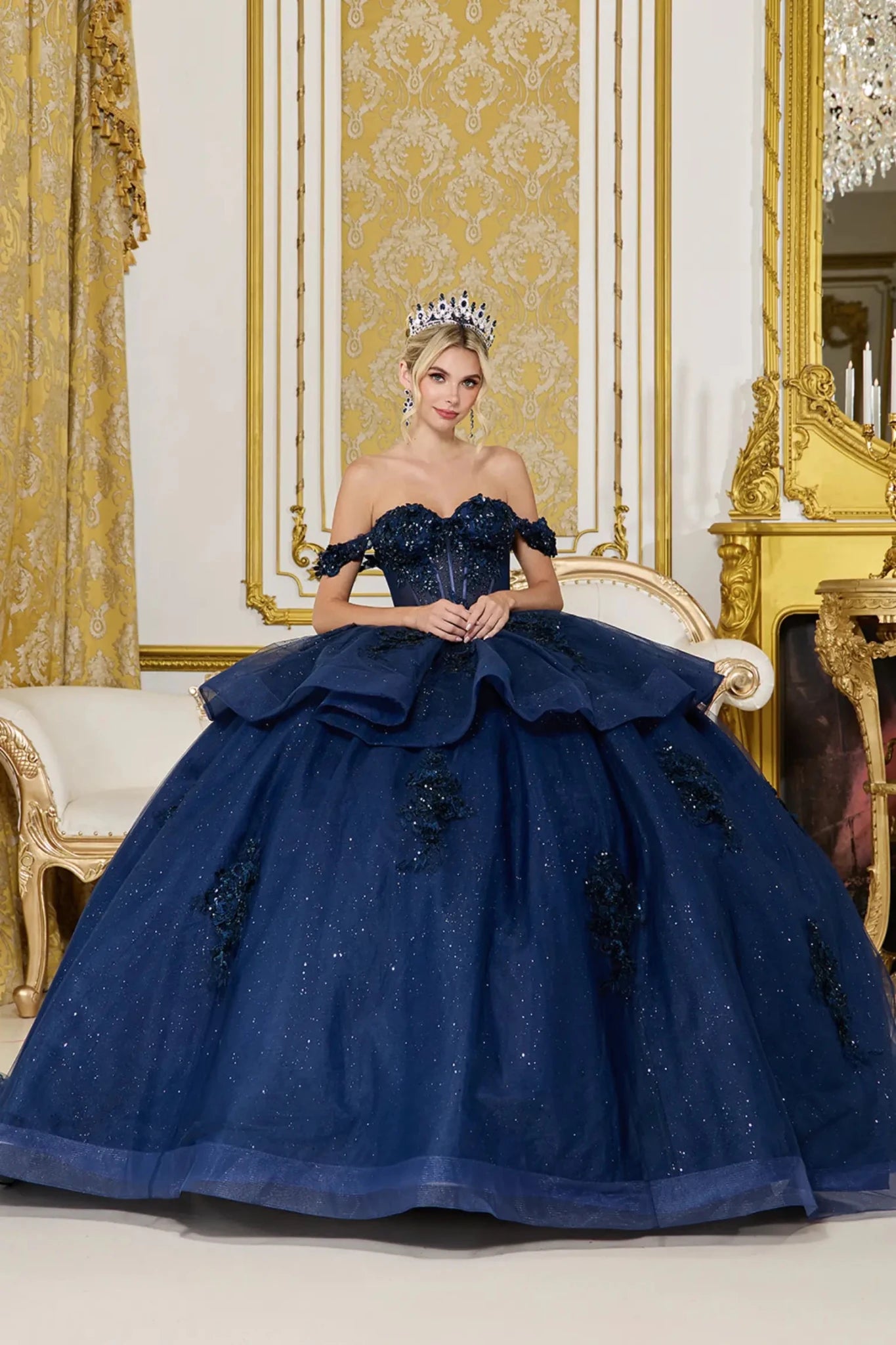 Front view of navy quinceañera ball gown with off-the-shoulder neckline, sweetheart corset bodice, layered glitter tulle skirt, and floral lace appliqués.