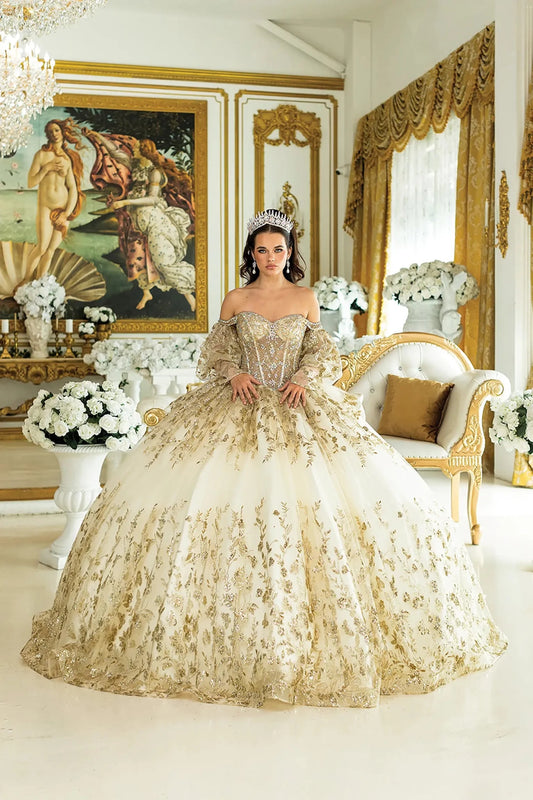 Woman standing front-facing in champagne quinceañera ball gown with off-shoulder sleeves, intricate embroidery, glitter accents, and voluminous full skirt