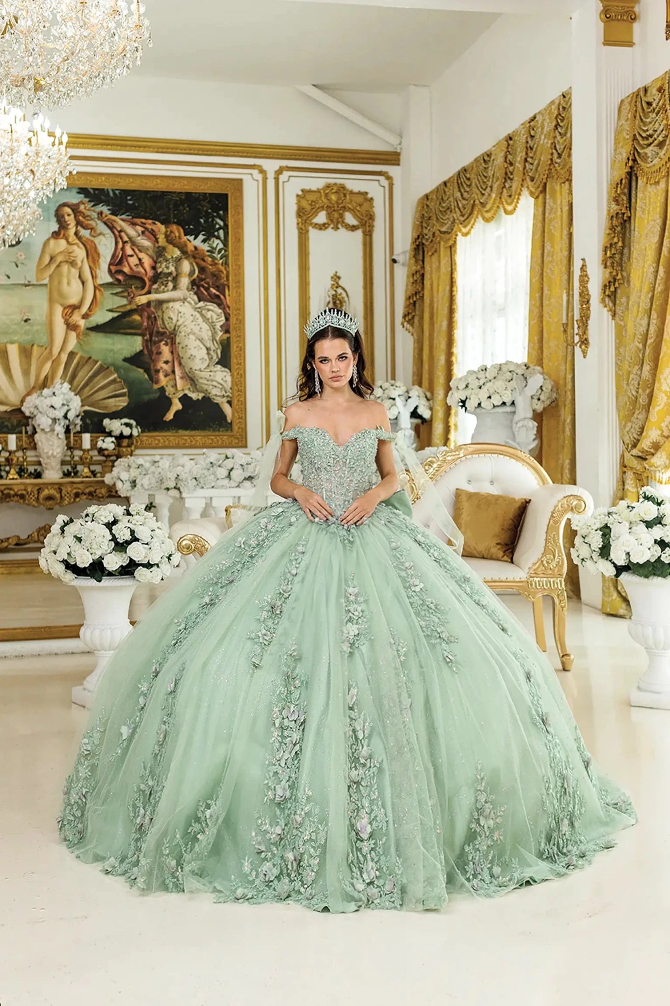 Woman standing front-facing in sage quinceañera ball gown with off-shoulder floral appliqués, fitted corset bodice, and voluminous sparkling tulle skirt