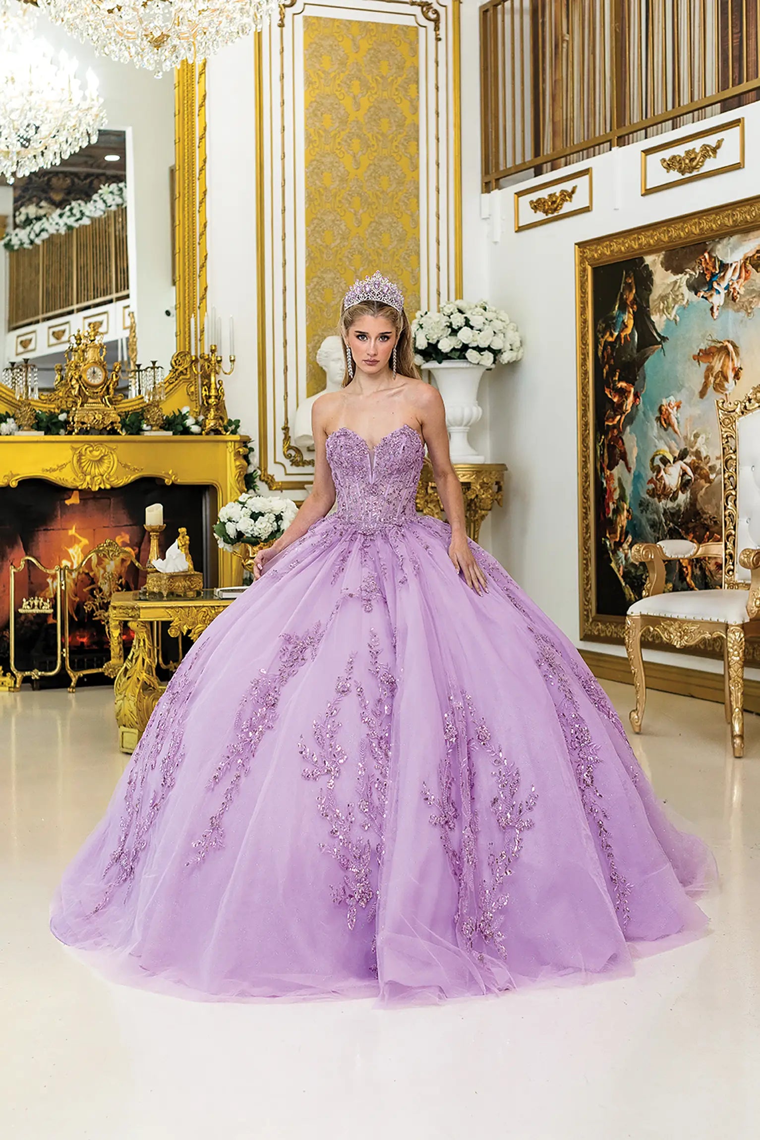 Front view of lilac quinceañera ball gown with sweetheart corset bodice, sheer structure, intricate lace appliqués, and a full tulle skirt in an ornate gold interior setting.