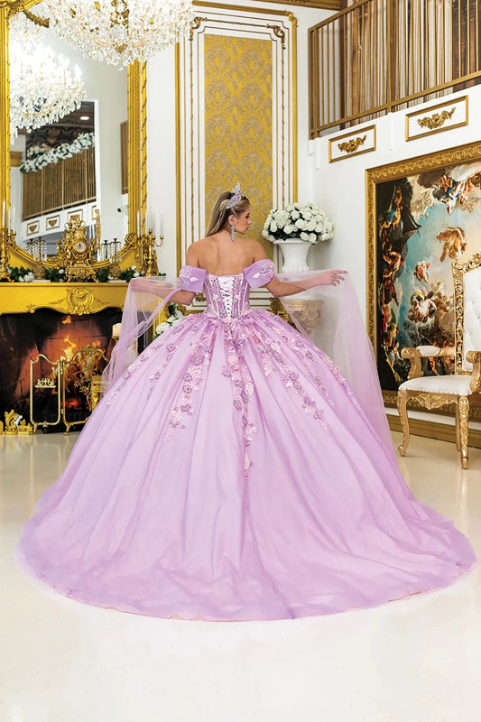 Woman standing back-facing in lilac quinceañera ball gown with off-shoulder sleeves, lace-up corset bodice, floral embroidery, glitter tulle overlay, and detachable sheer cape trailing behind