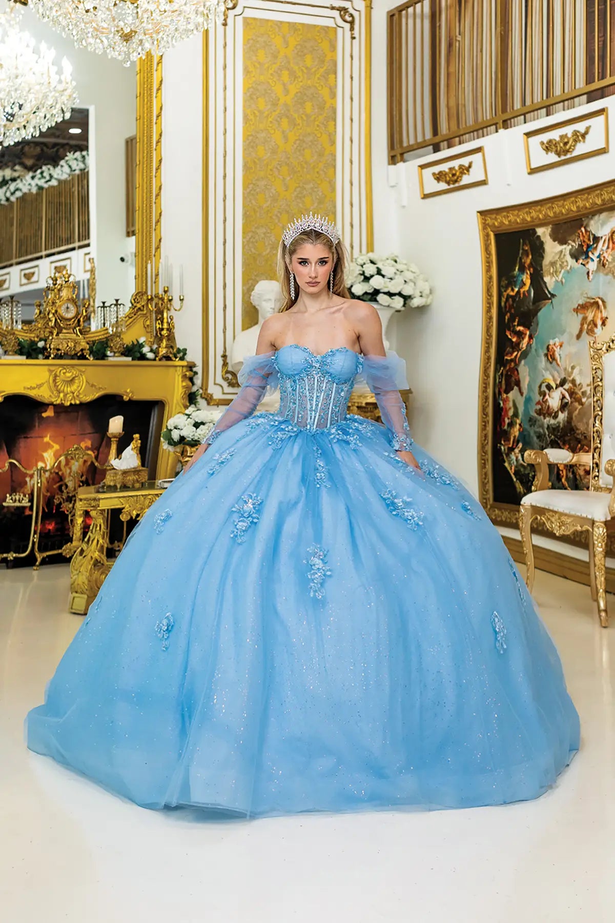Woman in a blue ball quince gown standing in an ornate room with gold decor.