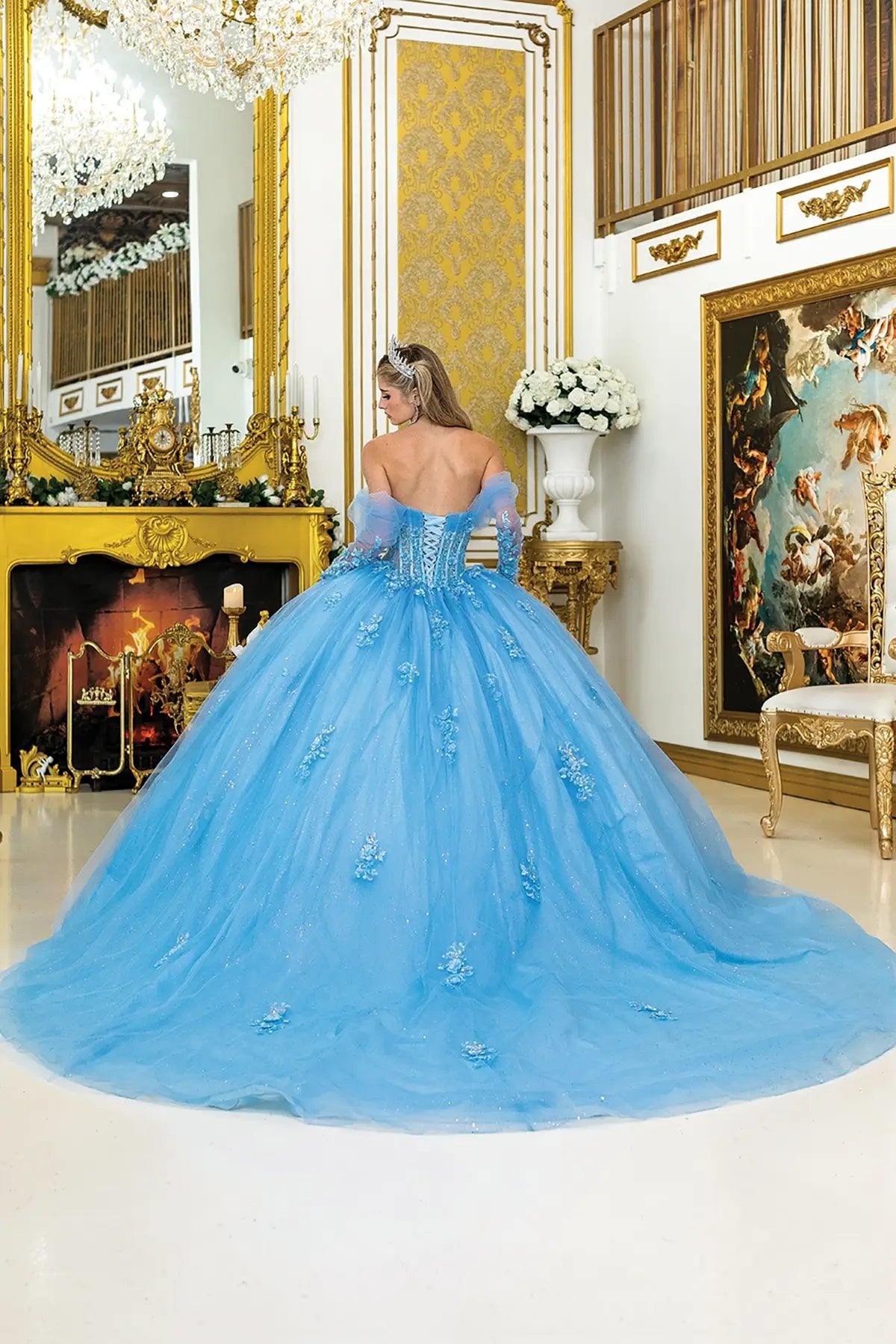 Woman in a blue quinceanera sweet heart gown standing in an opulent room with gold decor.