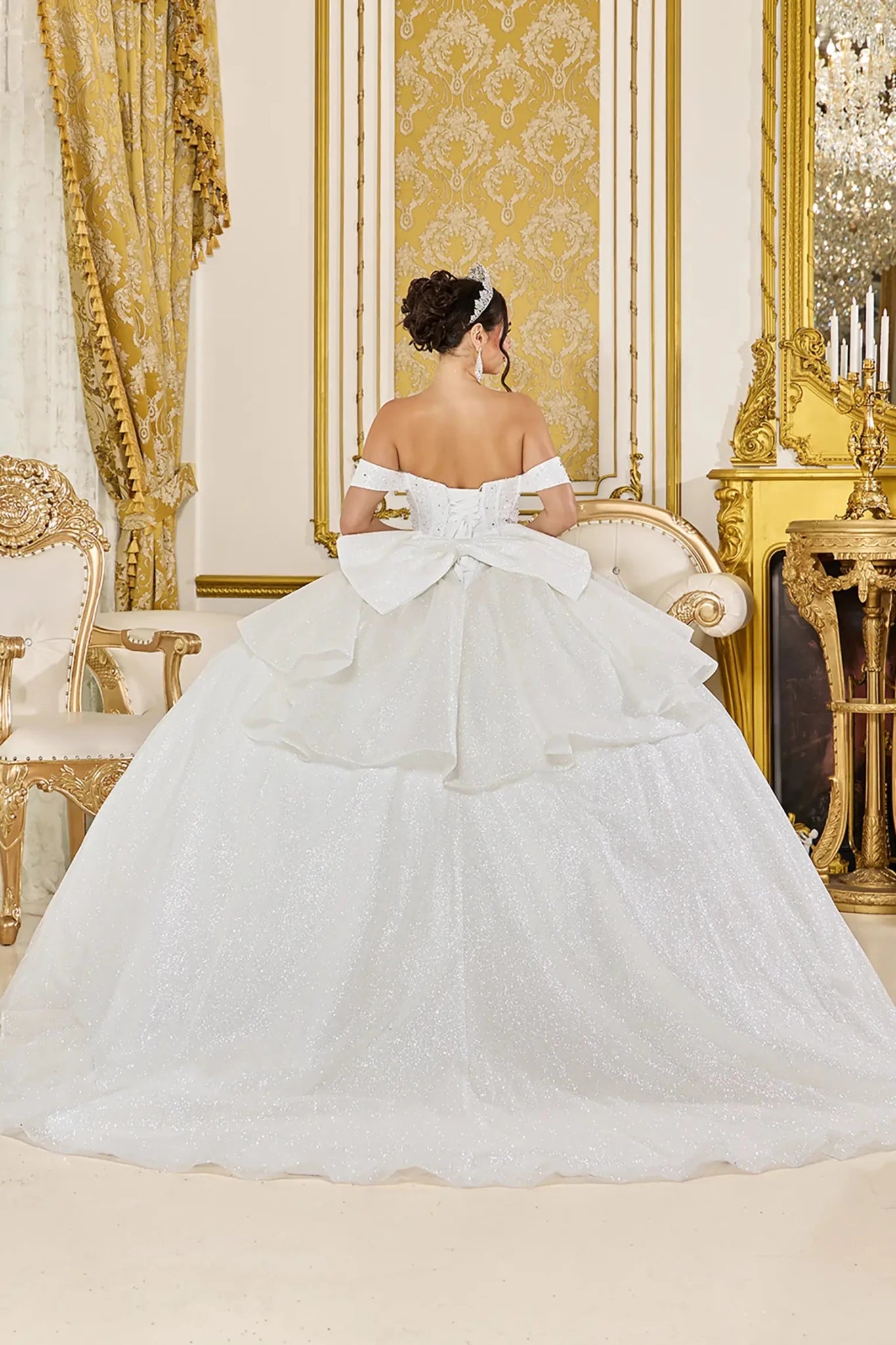 Off white quinceanera ball gown back view showing lace up corset back, oversized layered bow detail, shimmering tulle skirt, and sweeping train