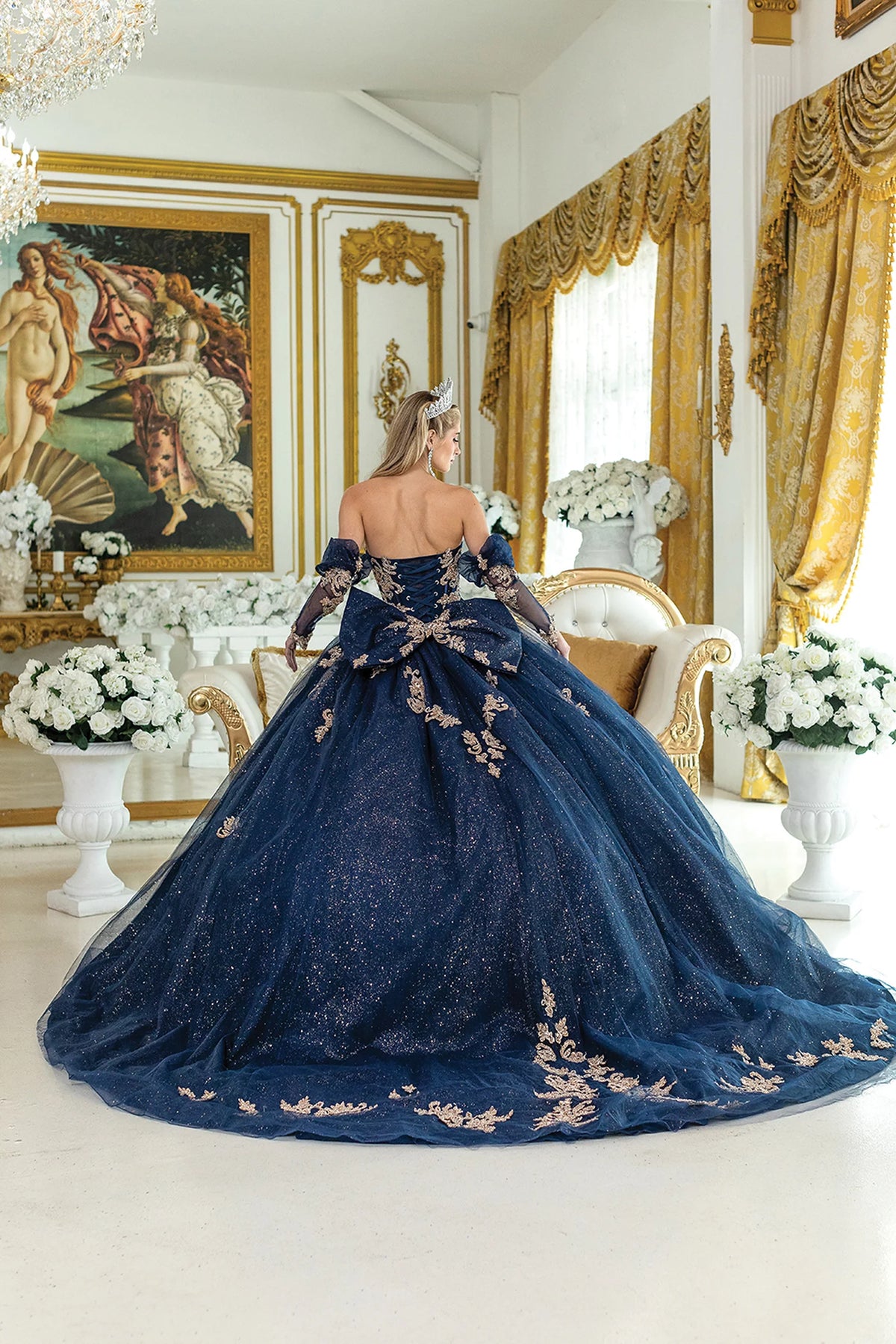 Revealing embroidered appliqués along its sweeping train, this Navy quinceañera ball gown is shown from the back.