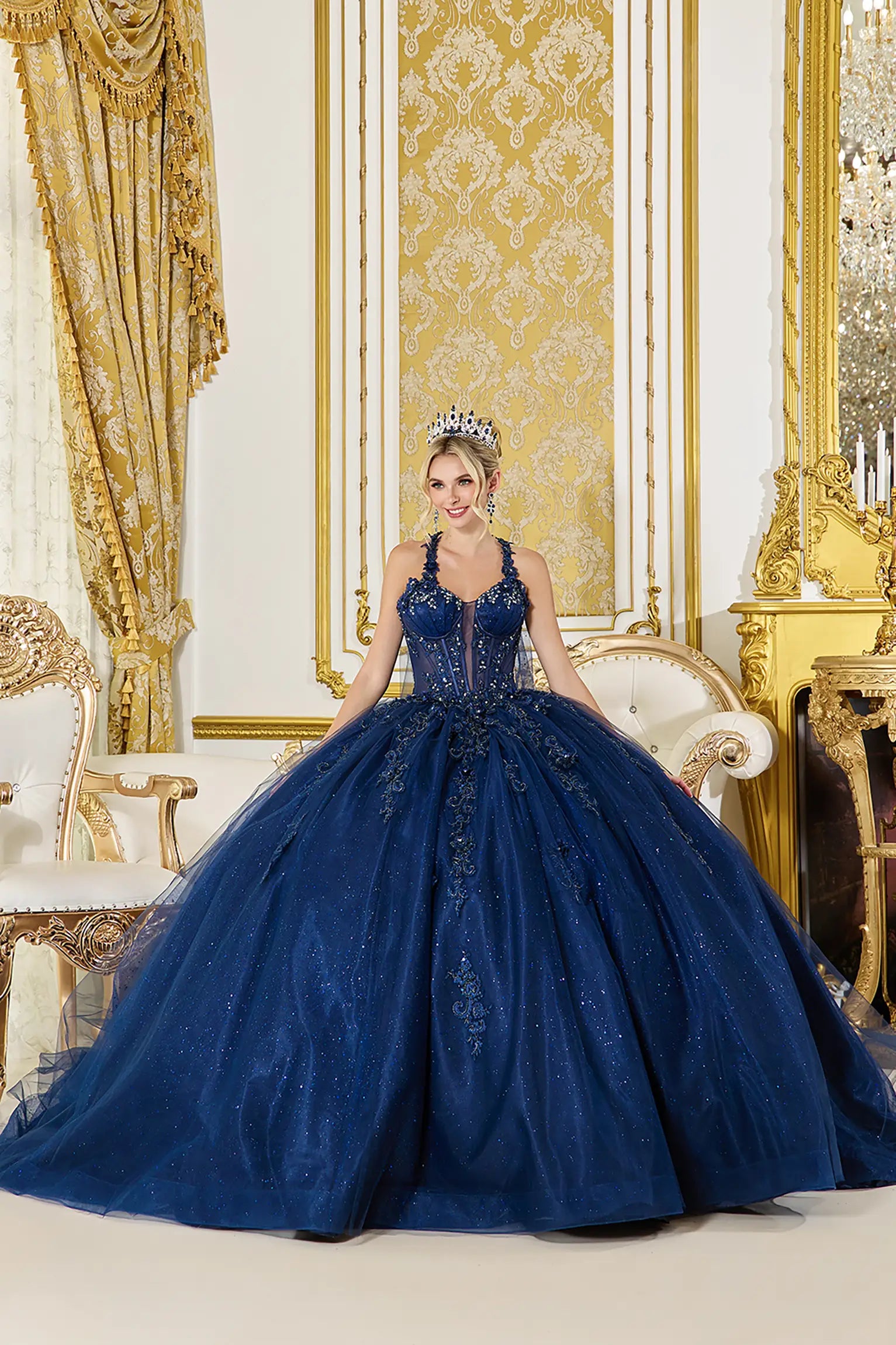 Front view: Navy blue quinceañera ball gown with embellished corset bodice, sheer illusion neckline, lace appliqués, and a voluminous glitter tulle skirt in a grand palace setting