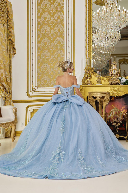 Woman in a light blue off quince gown with a large bow in an ornate room with gold decorations and a chandelier.