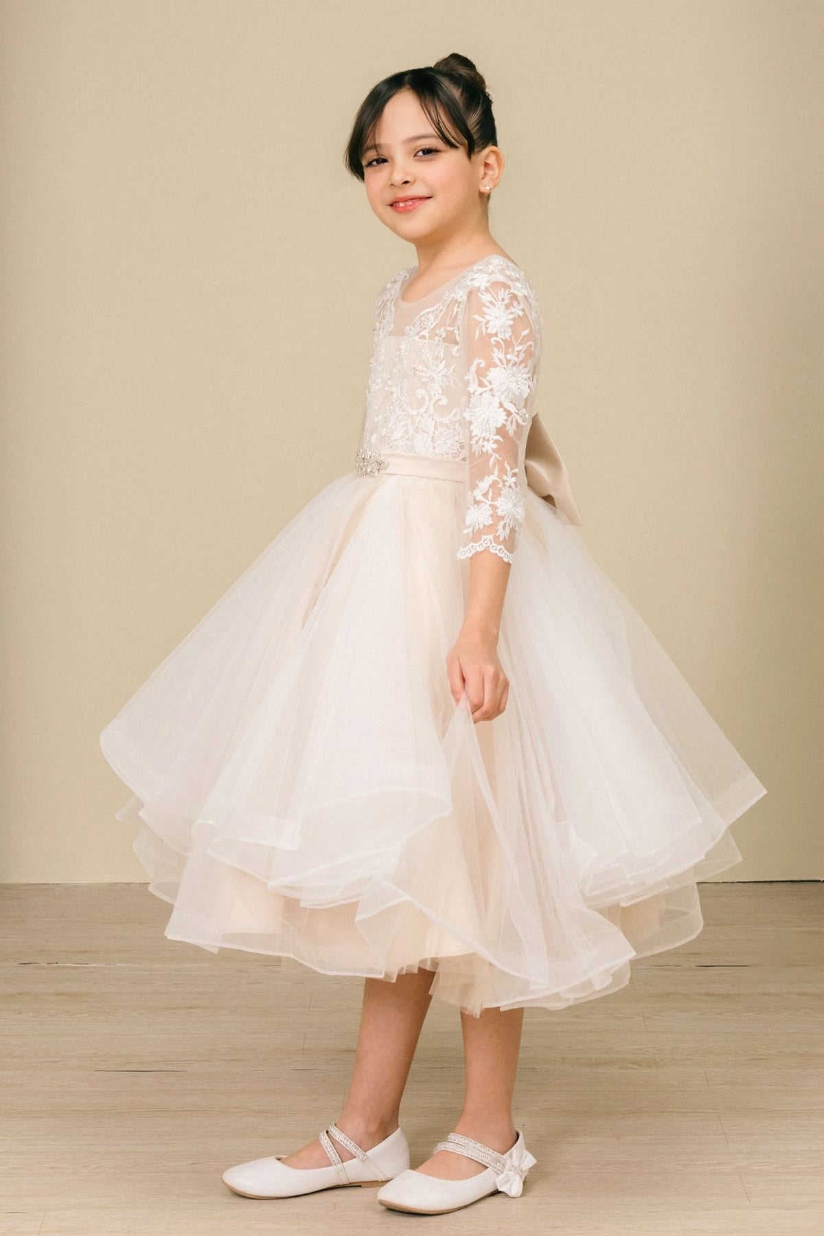 Detailed by a V-shaped lace back and large bow, the Champagne kids party dress reveals its construction.