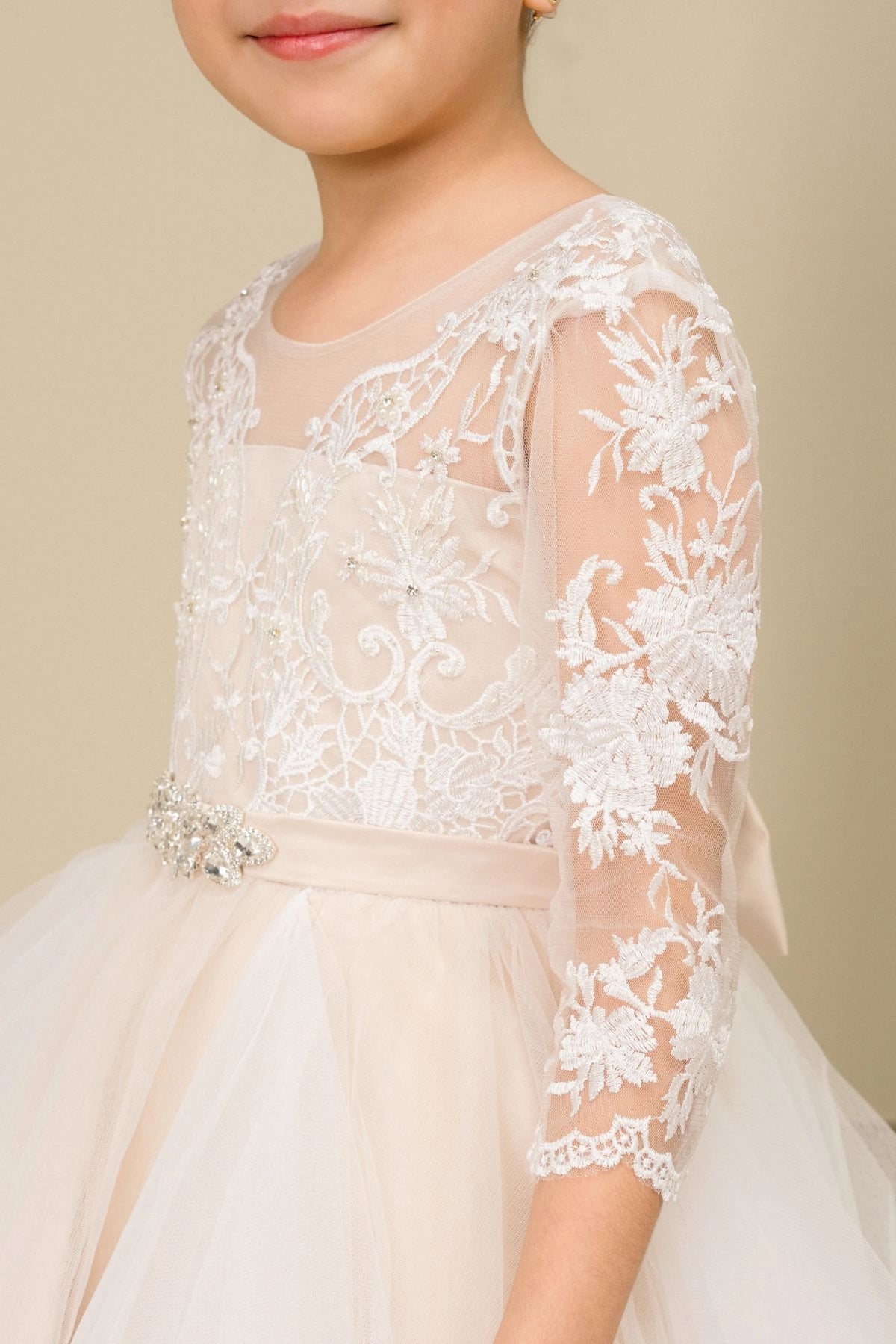 Designed details of sheer floral lace sleeves distinguish the Champagne kids party dress.