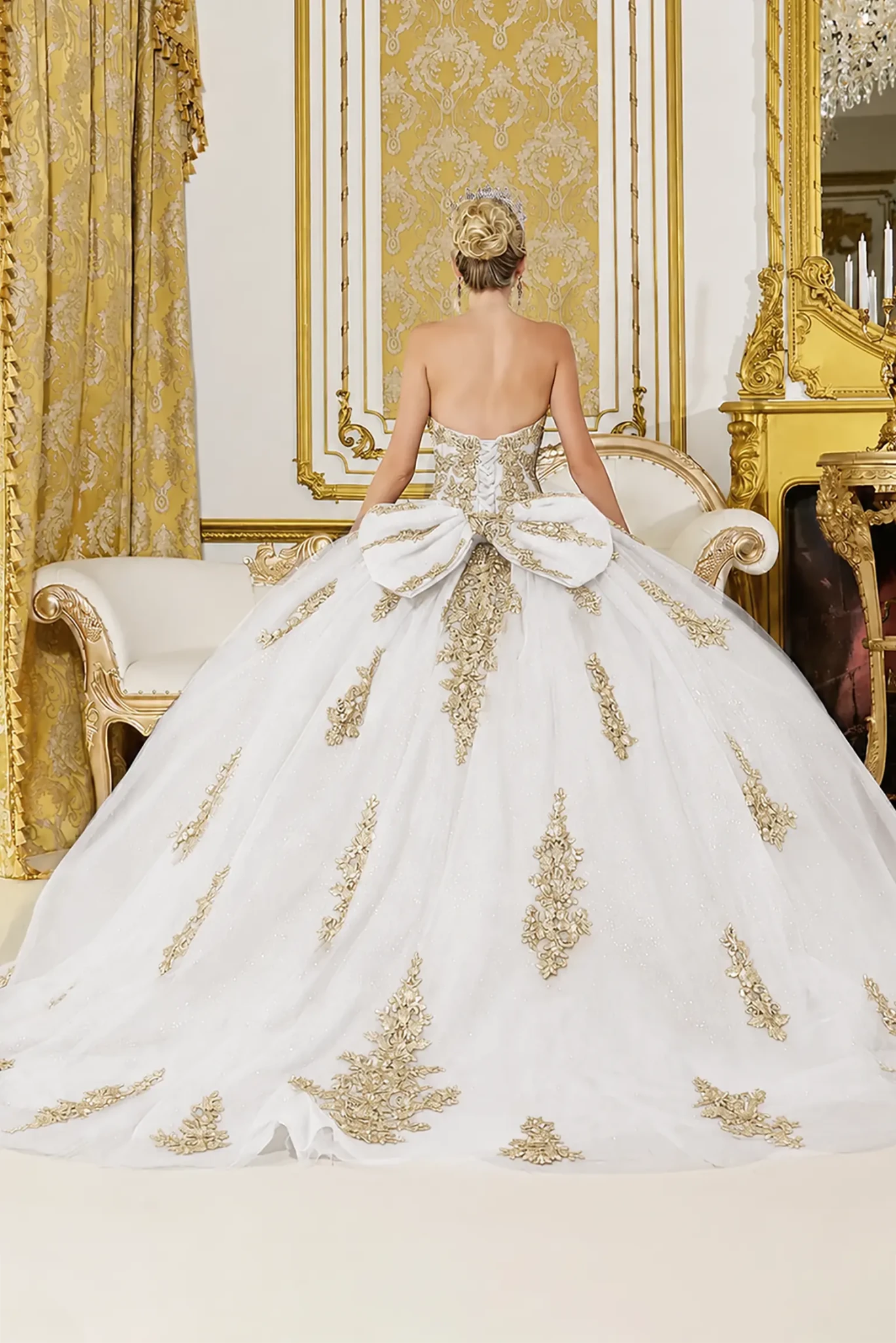 Back view of a woman wearing off-white quinceañera dress with lace-up corset, gold embroidery and bow detail