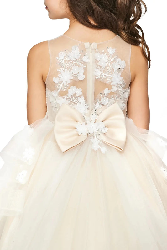 Back-facing in champagne high-low flower girl dress with lace-up bodice, lace appliqué accents, sequin bead details, and detachable train.
