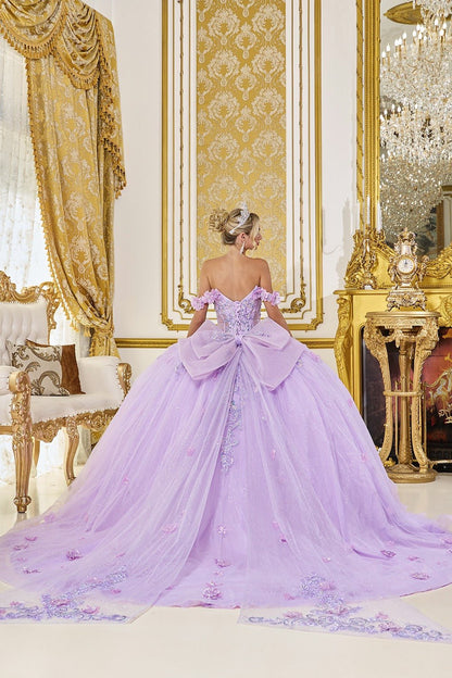 Woman in a lilac ball gown with a big back ribbon and train standing in an opulent room with gold decor.