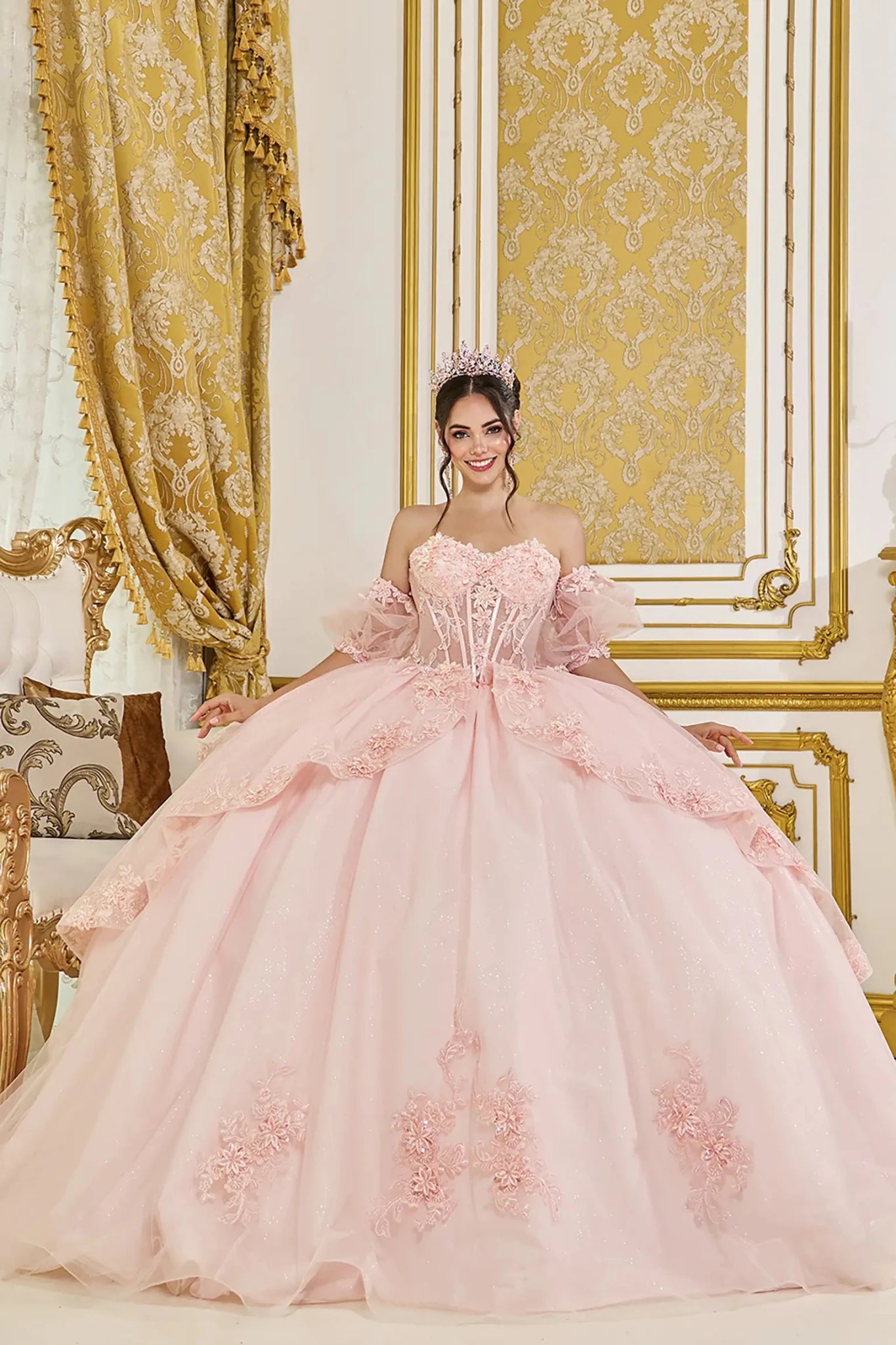 Blush quinceanera ball gown front view featuring sheer corset bodice, off the shoulder tulle sleeves, floral lace appliques, and full layered tulle skirt