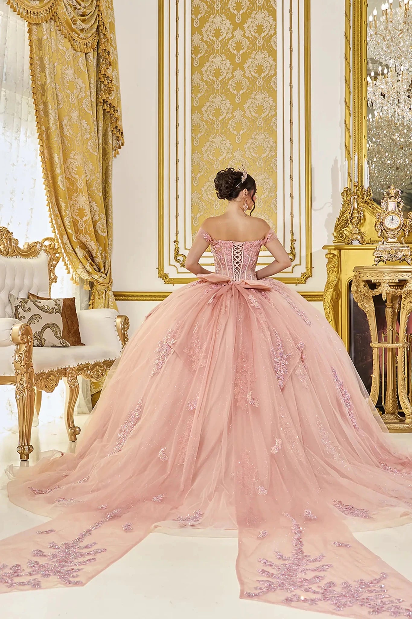 Back view of rose gold quinceañera ball gown featuring a lace-up corset back, soft bow accent, and long flowing tulle train with delicate applique detailing