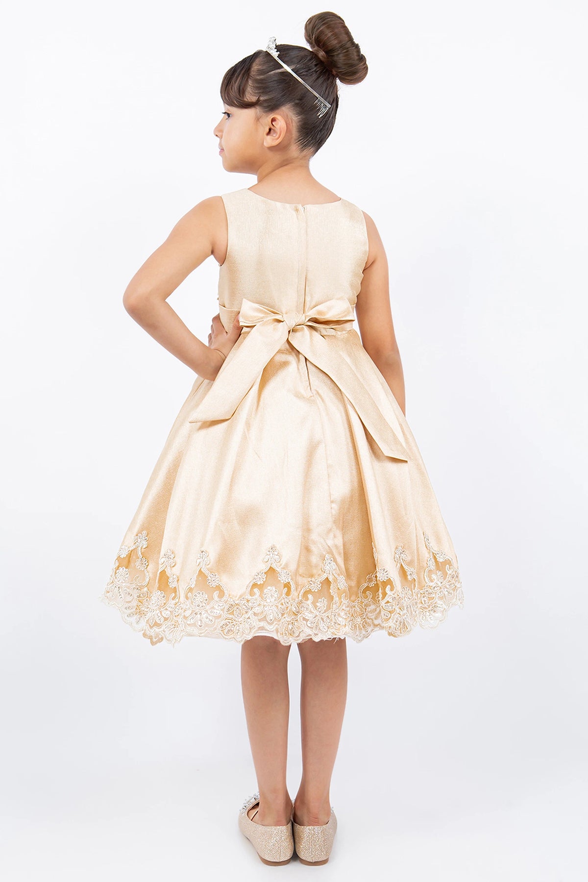 A Champagne flower girl dress showing large sash bow above the embroidered hem.