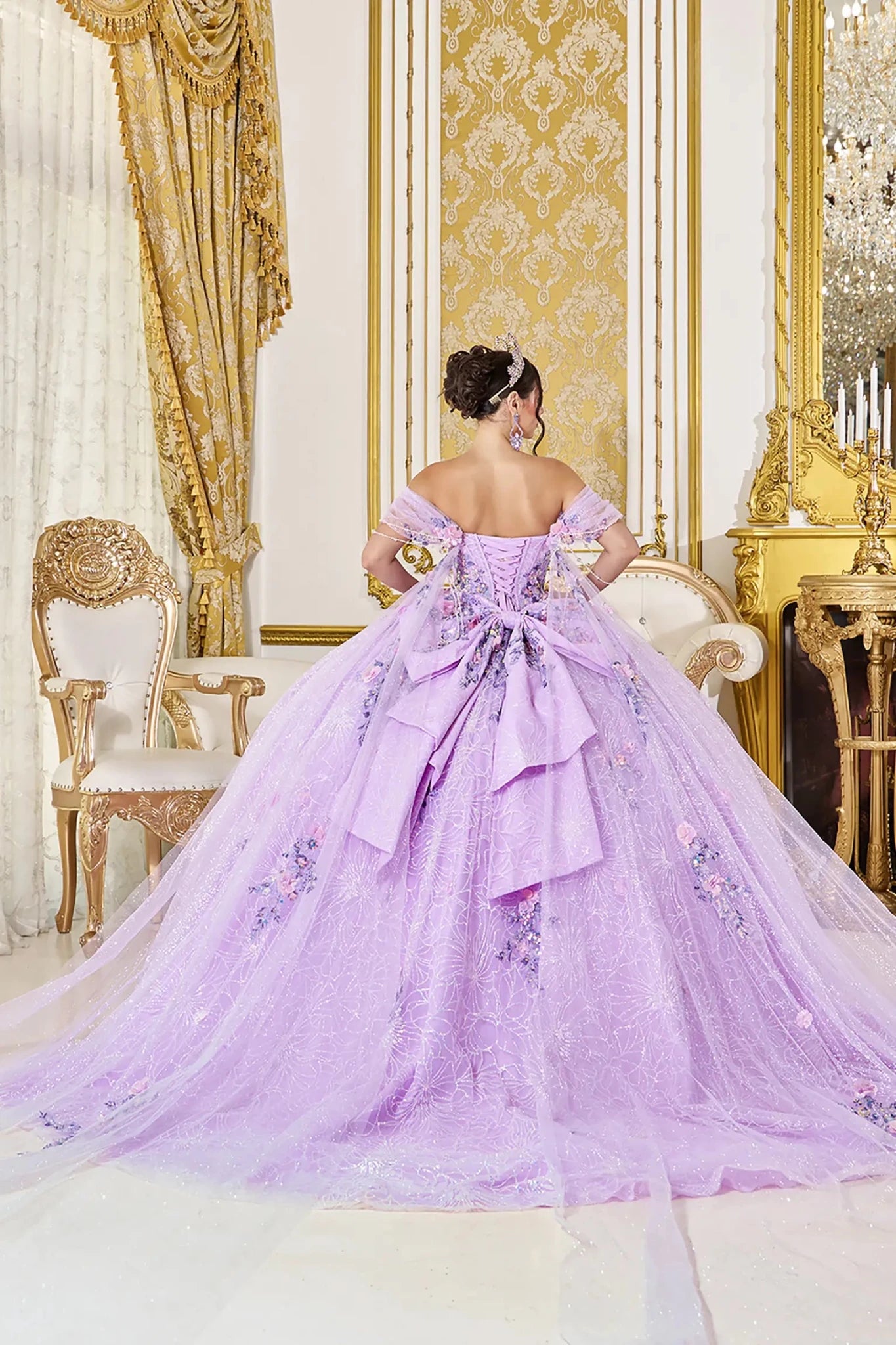 Back view of lilac quinceañera ball gown featuring lace-up corset back, layered bow detail with cascading tulle, off-the-shoulder straps, and voluminous embroidered tulle skirt.