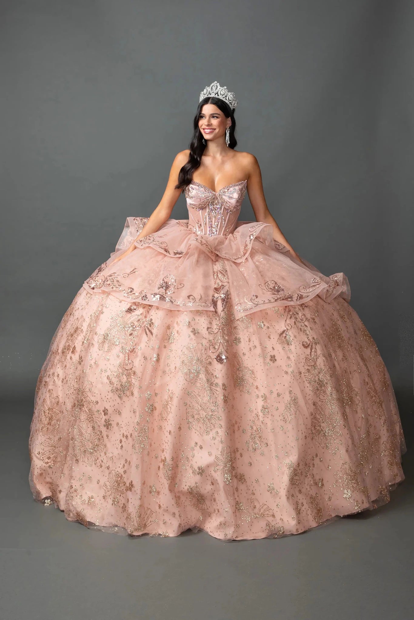 Woman in Rose gold strapless quinceañera ball gown with beaded corset and layered tulle skirt.
