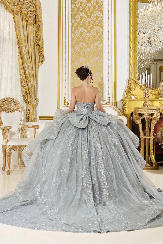 Back view of silver quinceañera ball gown featuring lace-up corset back, oversized bow accent, and full glitter tulle skirt with embroidered appliqués.