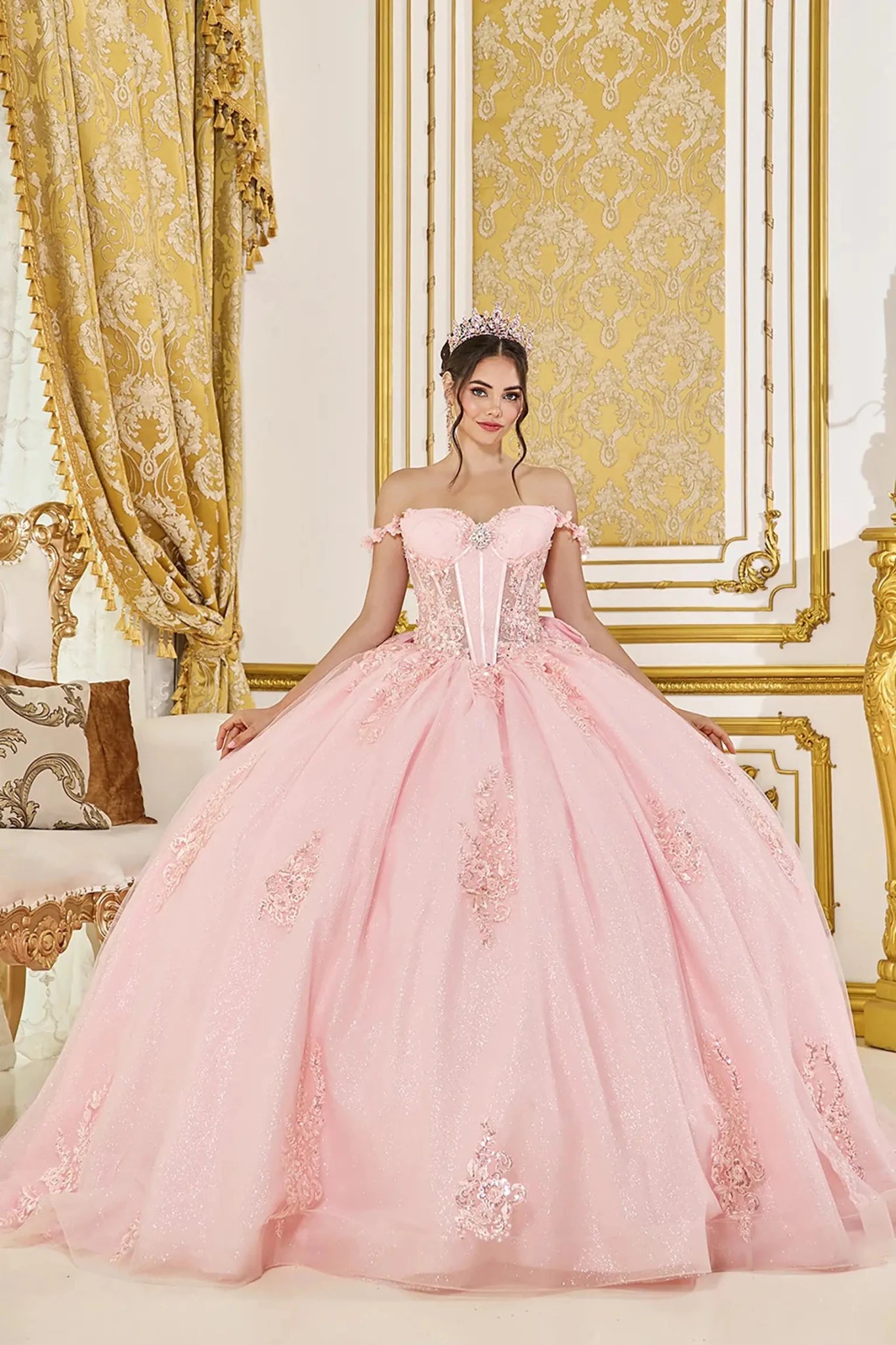 Woman wearing blush off-shoulder sweetheart quinceañera dress with embroidered corset bodice and glitter tulle full skirt